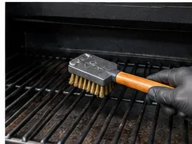A gloved hand cleaning black pellet-grill grates with a sturdy non-wire grill brush