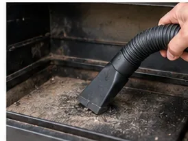 A shop-vac nozzle removing loose gray ash from the cold interior of a pellet grill