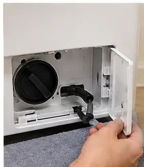 An open lower access panel on a front-load washer showing the drain-pump filter and small emergency drain hose