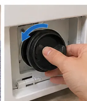 A hand turning a washing-machine pump filter clockwise to secure it inside the service opening