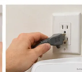 A hand reconnecting a washing machine power cord after the lower filter service has been completed