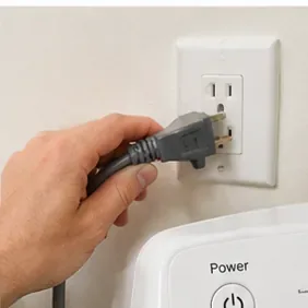 A hand unplugging a front-load washing machine from a wall outlet before filter maintenance