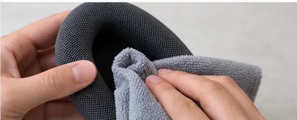 Hands gently wiping the woven surface of an AirPods Max cushion with a soft gray cloth