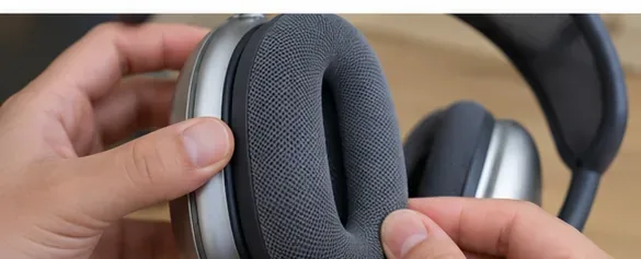 Hands placing a clean gray cushion back onto an AirPods Max ear cup
