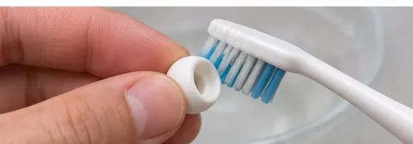 A white AirPods Pro ear tip held near the bristles of a small toothbrush