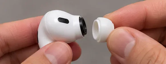 A hand holding an AirPods Pro earbud next to a detached white ear tip