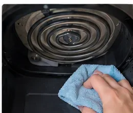 A microfiber cloth wiping the interior surface beneath an air fryer heating element.