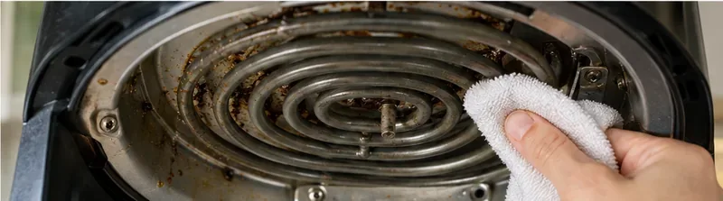 A soft damp cloth wiping grease from the accessible metal area around an air fryer heating coil.