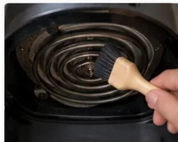 A soft-bristled brush gently cleaning food residue from an accessible air fryer heating element.