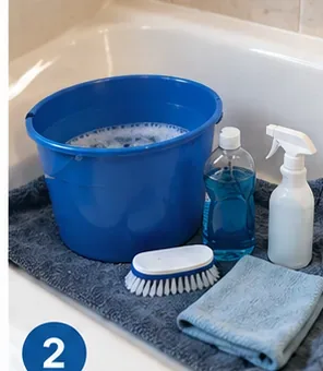 Bucket, mild cleaner, soft brush, spray bottle, and microfiber cloth arranged in a bathtub