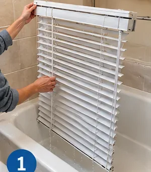 White horizontal blinds being positioned over an empty bathtub before cleaning