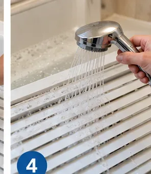 Handheld shower rinsing detergent from white blind slats in a bathtub