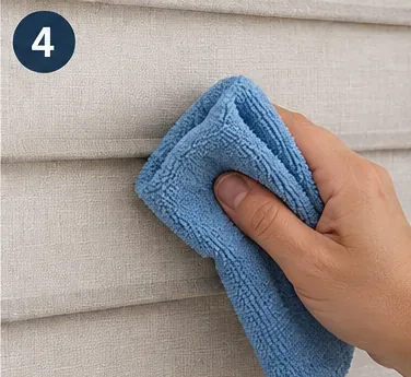 A hand holding a damp blue microfiber cloth lightly against a small area of beige fabric blinds