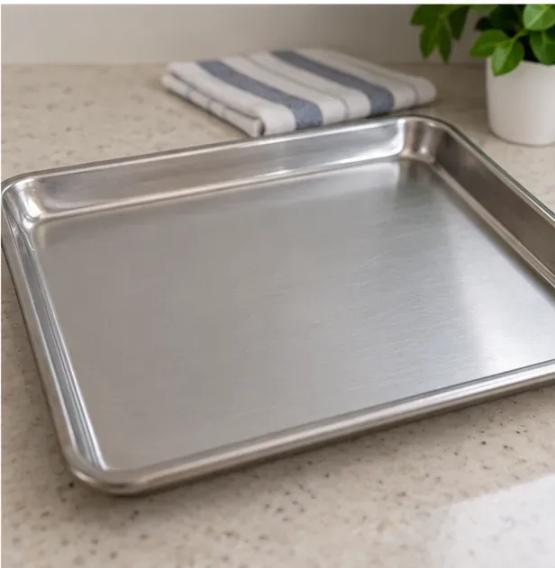 A clean dry bare-metal oven tray on a kitchen counter beside a folded towel
