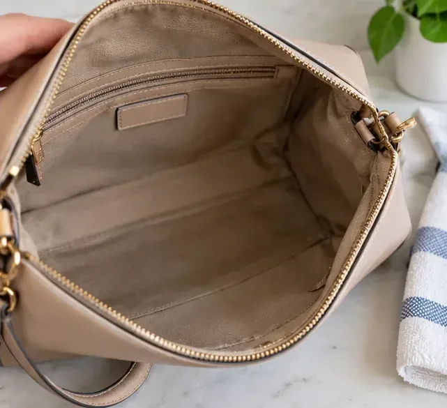A beige purse held open with a clean, dry interior and empty pockets visible.