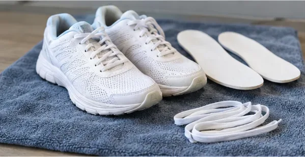 White running shoes, removable insoles, and laces laid separately on a towel to air dry.