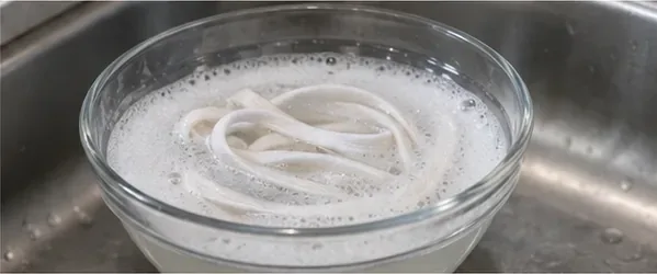 White shoelaces soaking in a glass bowl of lightly soapy water.