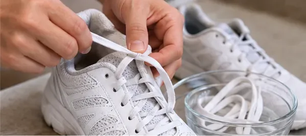 Hands removing white laces from a white running shoe with a bowl beside it.