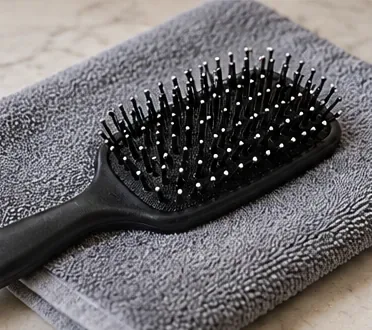 A clean black paddle hairbrush resting on a dry gray towel after washing