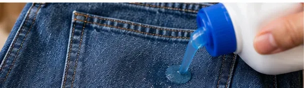 Liquid laundry detergent being applied directly to a small gum-residue mark on blue denim