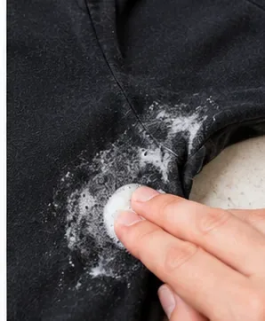 Fingers gently working a foamy pretreatment into the deodorant-marked underarm of a black T-shirt