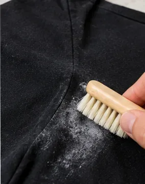 Soft clothes brush being used on white deodorant residue at the underarm of a black shirt