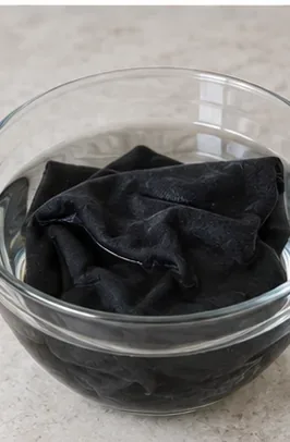 Black shirt soaking in a clear glass bowl during an optional pretreatment for stubborn underarm residue