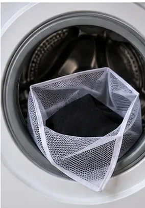 Black shirt in a mesh wash bag being placed into the drum of a front-loading washing machine