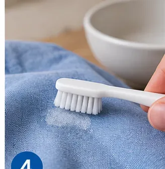 Soft white brush gently working a treated glue residue on blue fabric