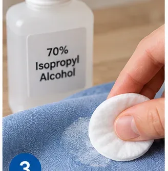 Cotton pad beside a bottle labeled 70 percent isopropyl alcohol over a glue-marked garment