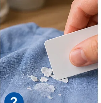 Dull plastic card gently scraping dried glue flakes from blue fabric