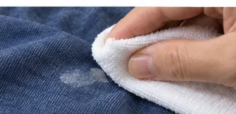 A white cloth blotting a softened glue mark on blue fabric.