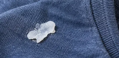 A dried translucent glue spot resting on blue fabric before treatment begins.