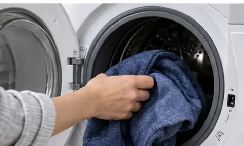 A blue garment being loaded into a front-loading washing machine.