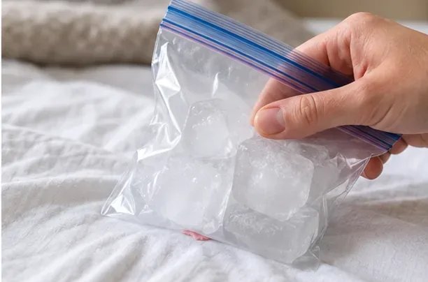 A hand holding a sealed bag of ice cubes against chewing gum on a white sheet