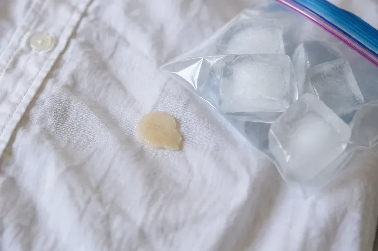 A bag of ice beside a hardened beige wax spot on a white shirt