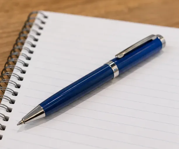 A blue refillable pen reassembled and resting on a lined notebook, ready for a writing test