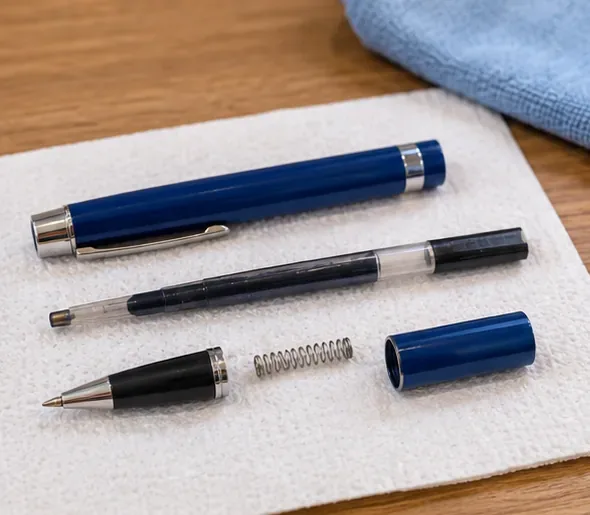 A refillable blue pen opened on a towel with the barrel, ink refill, metal tip section, and spring laid out separately