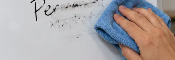 A blue microfiber cloth wiping marker residue from a white dry-erase board