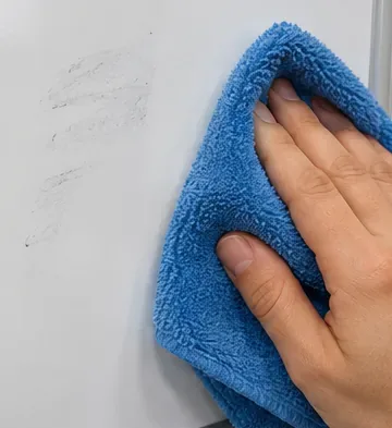 A microfiber cloth wiping faint remaining gray residue from a dry-erase board