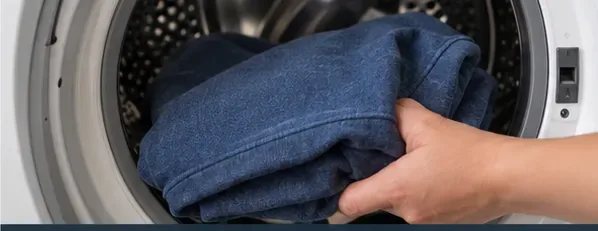 Blue garment being placed into a front-loading washing machine after adhesive pretreatment