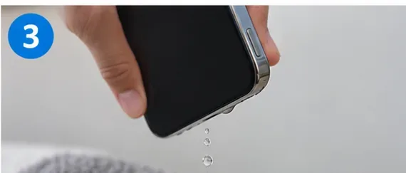 A smartphone held with its charging port facing downward while drops of water fall away.