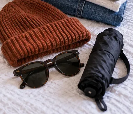 Rust knit beanie, sunglasses and a compact black umbrella grouped together for quick access during changing weather