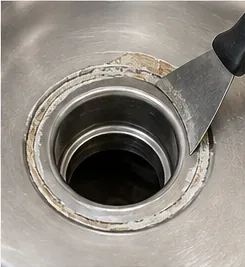 Putty knife working around old sealant at the rim of a kitchen sink drain opening