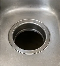 Clean stainless-steel kitchen sink drain opening after the old strainer and sealant have been removed