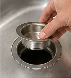 Hand lifting a stainless-steel basket-strainer body out of a kitchen sink drain opening