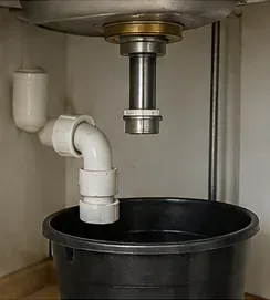 Bucket positioned below disconnected kitchen sink drain plumbing inside the sink cabinet