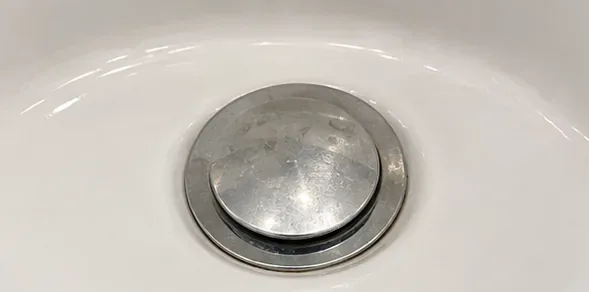 Close-up of a chrome push-style sink stopper seated in a white bathroom basin