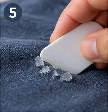 A smooth plastic scraper removing chilled glue fragments from blue woven fabric