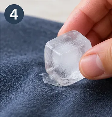 An ice cube being held over remaining hardened glue on blue fabric
